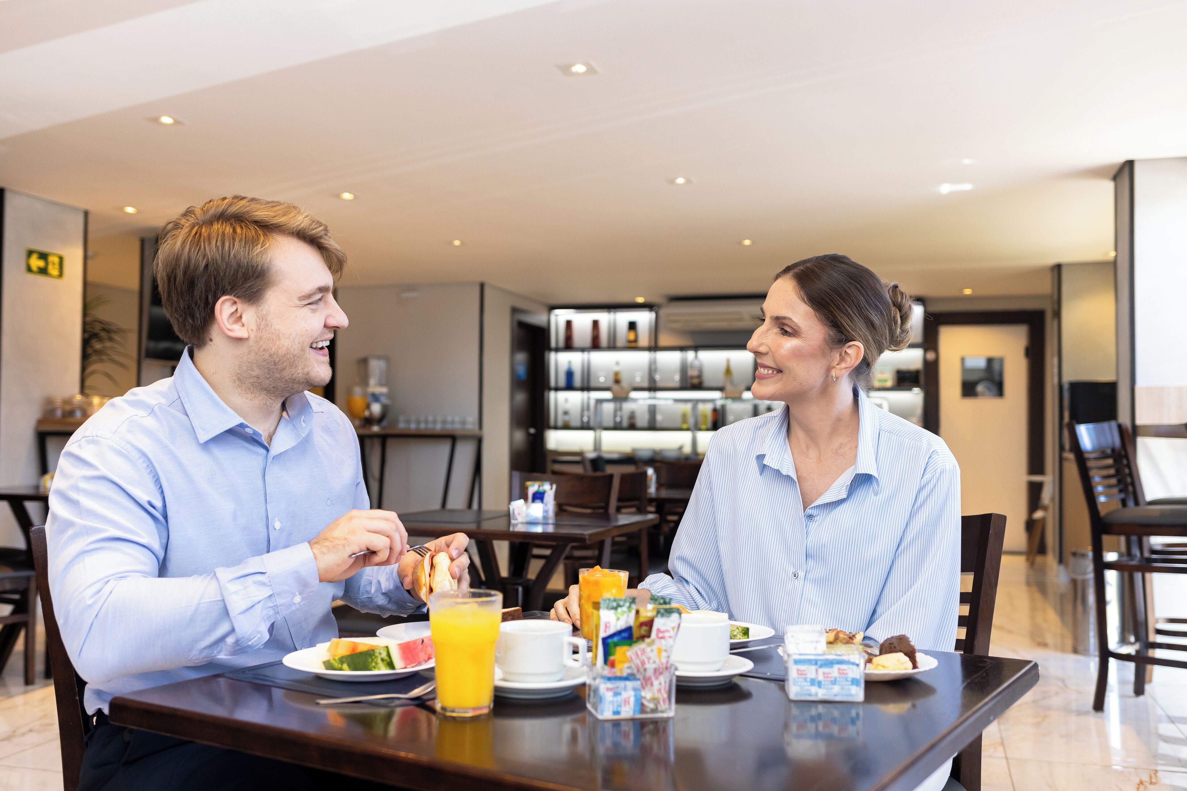 Comedor con una mesa dispuesta para dos personas, que incluye elementos para el desayuno como tostadas, fruta y jugo.