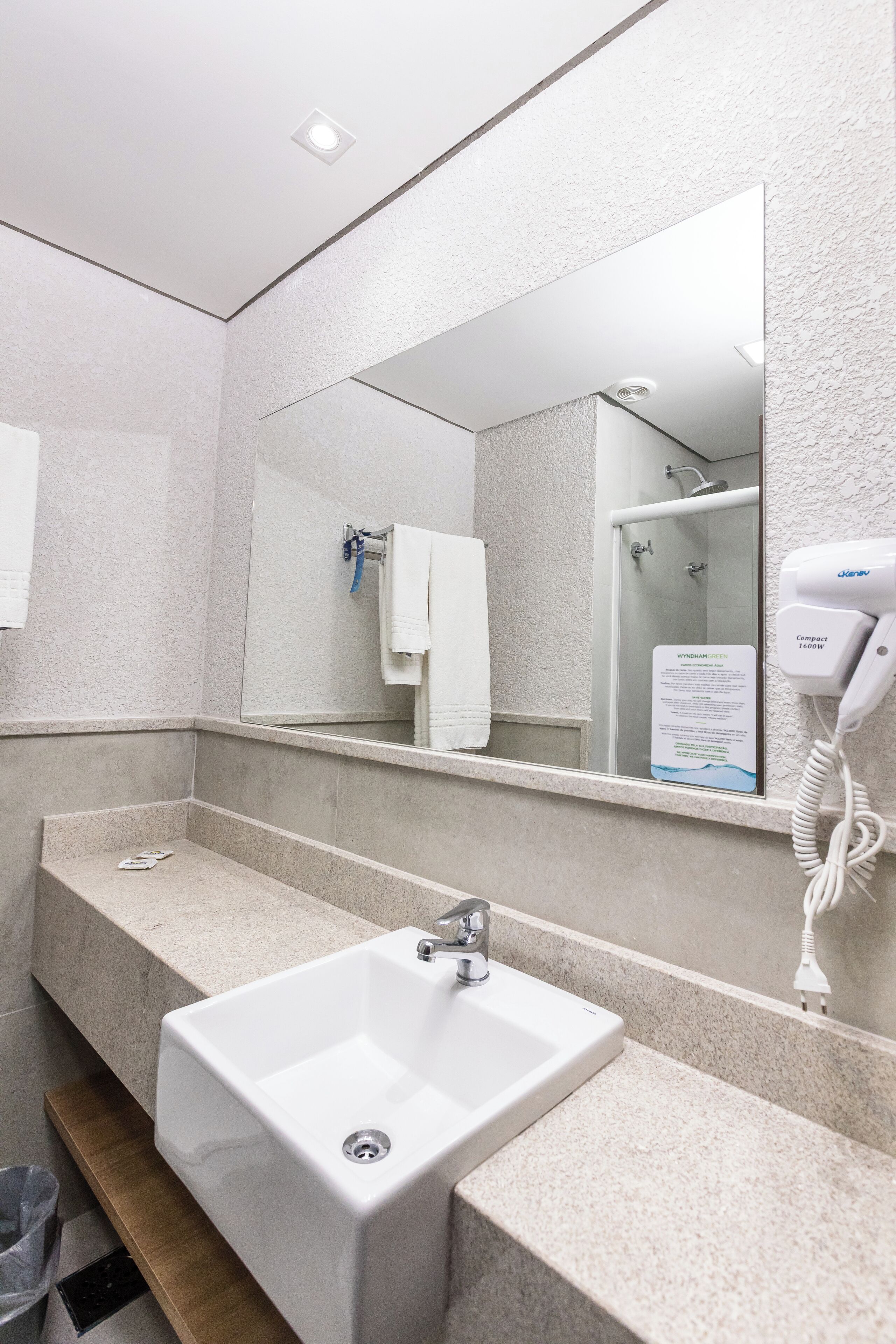 A bathroom with a white sink, a mirror, and a handheld hair dryer.
