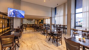 A spacious hotel lobby with a large flat-screen TV mounted on the wall, a bar area with shelves and bottles, and a seating area with multiple tables and chairs. - Days Inn By Wyndham Cascavel (Cascavel)
