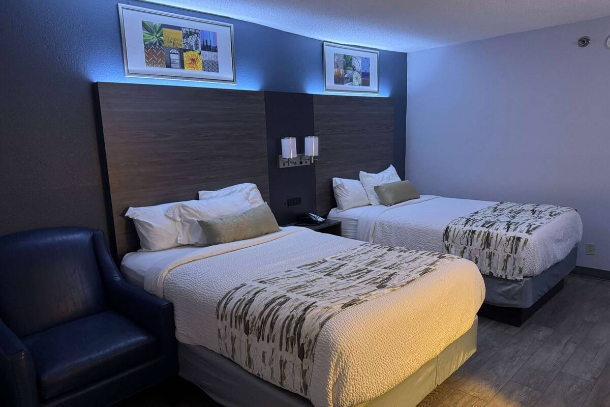 Hotellihuone, jossa on kaksi sänkyä, tuoli ja seinällä kehystetty taideteos.