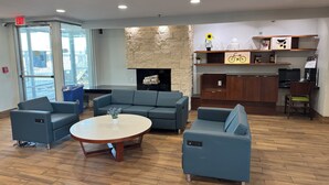 A modern lounge area with a stone fireplace, a round table, and blue seating. - Baymont By Wyndham Dayton North (Dayton)