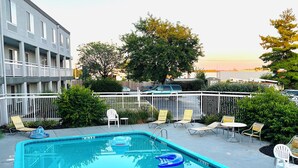 A rectangular swimming pool with a blue edge, surrounded by white railings. There are lounge chairs and a small table near the pool. - Baymont By Wyndham Dayton North (Dayton)