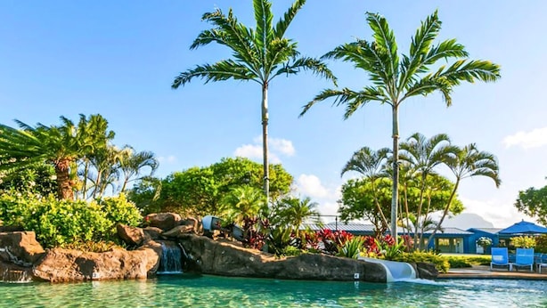 A clear pool with a waterfall, surrounded by palm trees and tropical plants. - Five Bed, Five Bath Tropical Paradise With A/C, Hot Tub, & Beach Walk (Koloa)