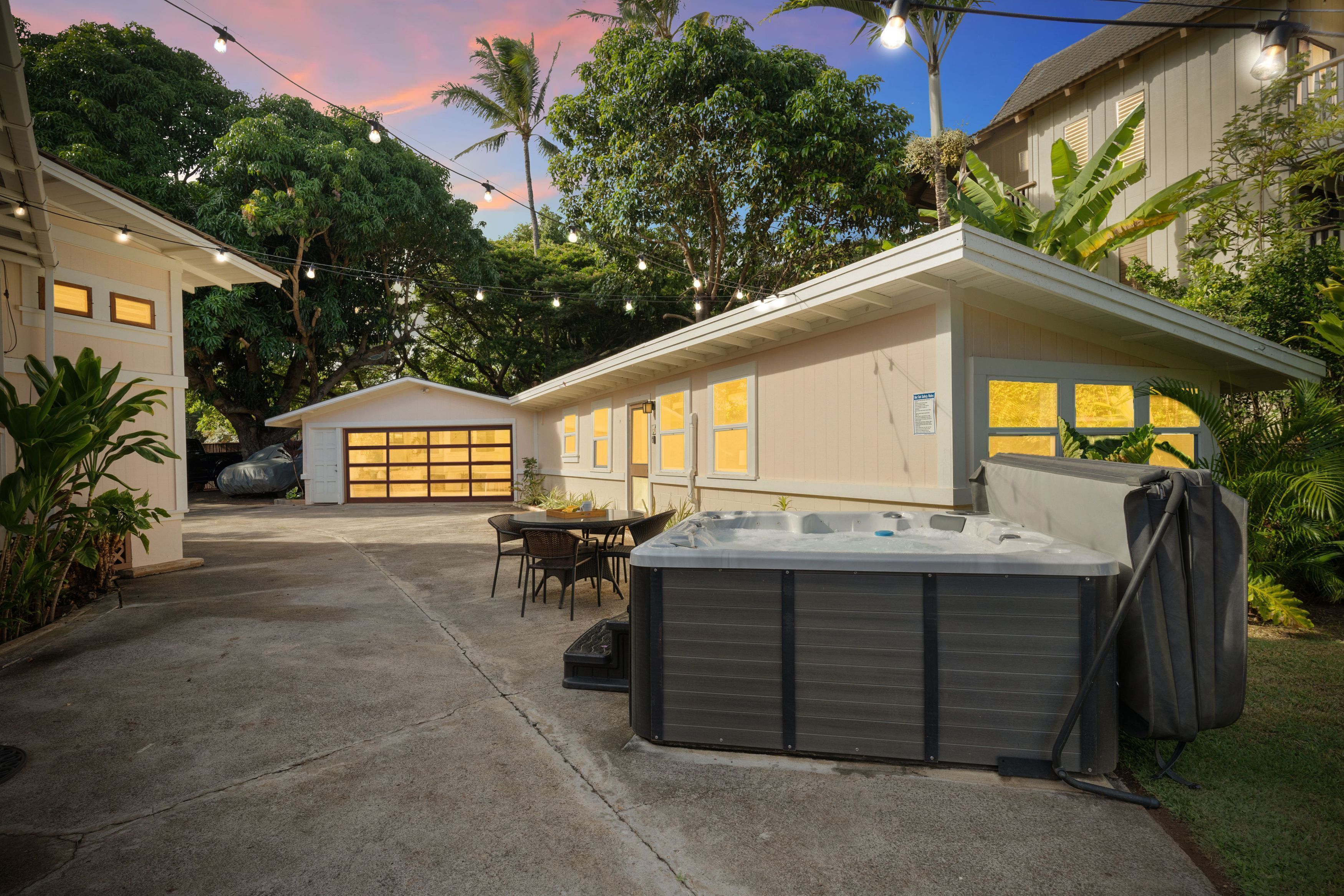 A residential backyard with a hot tub, a covered patio table, and a garage.