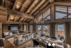 Amplia sala de estar con techo de madera, ventanas grandes, chimenea y comedor con una mesa larga dispuesta para seis personas.