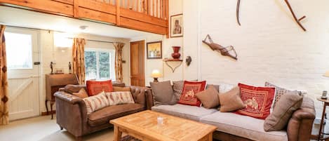 A cozy living room with a wooden ceiling, a brown leather sofa, a wooden coffee table, and a patterned rug.
