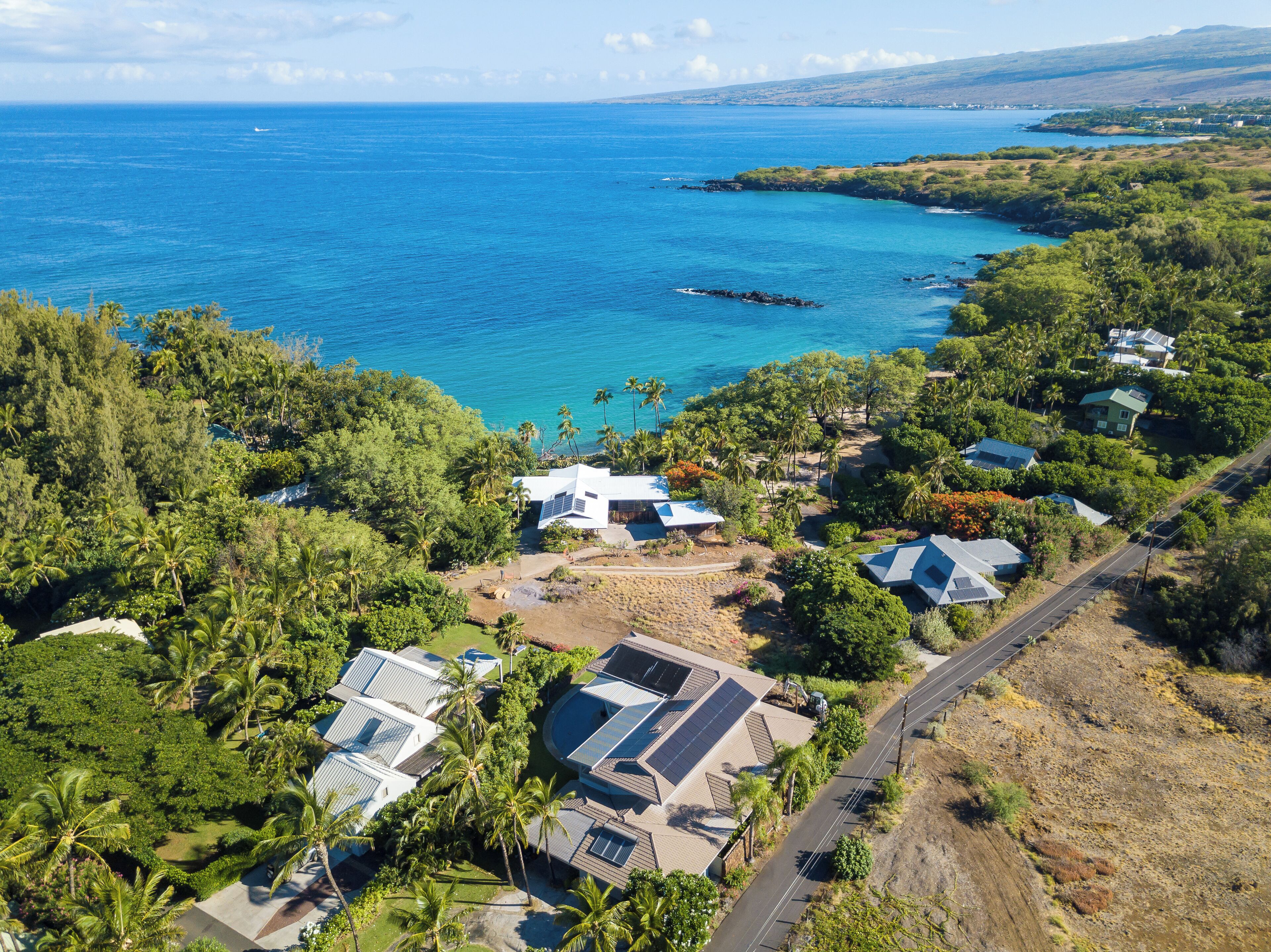 An aerial view of a coastal residential area with houses, solar panels, and a clear view of the ocean.