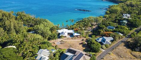 An aerial view of a coastal residential area with houses, solar panels, and a clear view of the ocean.