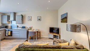 A modern living space with a kitchen, dining area, and a cozy seating area with a flat-screen TV and a floor lamp.
