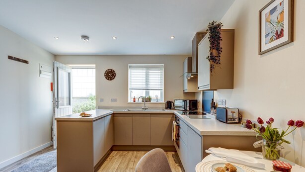 A modern kitchen with a central island, a dining area with a table and chairs, and a view of the outdoors through the window.