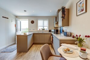 A modern kitchen with a central island, a dining area with a table and chairs, and a view of the outdoors through the window. - Highlander Barn I Oxfordshire Holiday Let | 1 Bed & Sleeps 2 (Witney)