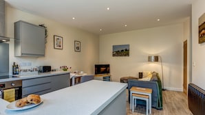 A modern kitchen with a central island, a dining area with a sofa, and a TV.