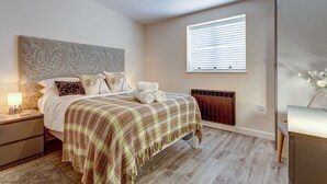 A bedroom with a bed, nightstands, a radiator, a window with blinds, and a desk with a chair.