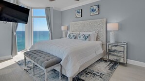 Quarto moderno com uma cama grande, ventoinha no teto, vista para o oceano e televisão de tela plana.