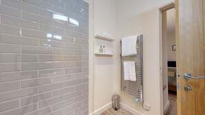 Ein Badezimmer mit grauen Fliesenwänden, einem Handtuchhalter mit Handtüchern, einer kleinen Ablage für Toilettenartikel und einer Tür mit Griff.