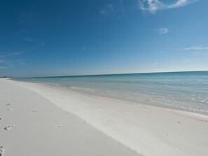 A wide, white sandy beach with gentle waves lapping at the shore under a clear blue sky. - Updated First Floor Condo, Close to Pool, Free Beach Service (Destin)