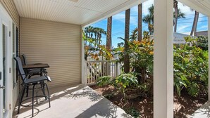 A covered porch with a table and chairs, surrounded by tropical plants and palm trees. - Updated First Floor Condo, Close to Pool, Free Beach Service (Destin)