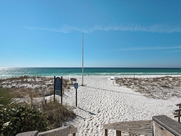 A sandy beach with a wooden fence, a signpost, and a lifeguard tower.