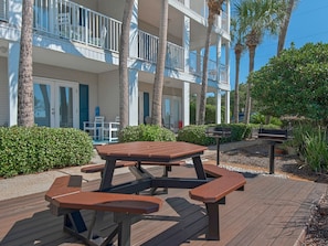 Enjoy a meal on the beachfront deck with a picnic table and benches, surrounded by lush greenery and palm trees.