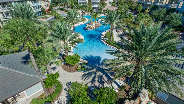 Un resort con piscina central, edificios de varios pisos y palmeras.