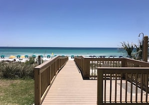 A wooden boardwalk leading to a beach with umbrellas and a sign welcoming visitors. - Gulf Front, Gated Community (Destin)