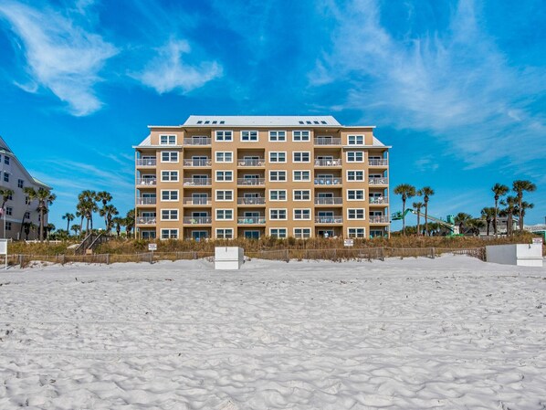 A multi-story hotel with a flat roof and balconies, located on a sandy beach with palm trees. - Gulf Front, Gated Community (Destin)