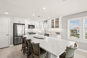 A modern kitchen with white cabinetry, stainless steel appliances, and a large island with bar stools. - Gulf Front, Gated Community (Destin)