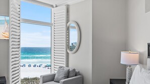 A bedroom with a view of the beach, a round mirror, a bedside lamp, and a grey armchair. - Gulf Front * Endless Beach Views * Private Balcony * Pool, Hot Tub, Tennis (Destin)