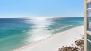 A beach view from a building with large windows, a clear sky, and the ocean.