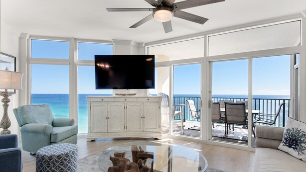 A spacious living room with a large TV, a ceiling fan, and a view of the ocean.