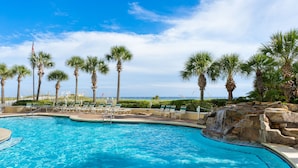 A swimming pool with palm trees, lounge chairs, and a waterfall feature.