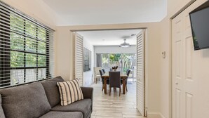 A modern living room with a grey sofa, a dining table with chairs, and a TV mounted on the wall. - 🌴🐠🍹Tropical Beachside Pool House!  Live your best life! (Pompano Beach)