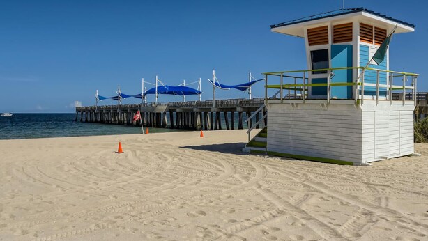 A lifeguard tower on a sandy beach with a pier extending into the water. - 🌴🐠🍹Tropical Beachside Pool House!  Live your best life! (Pompano Beach)