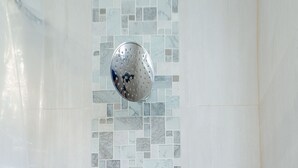 Et brusebad med væg af mosaikfliser og brusehoved i krom.