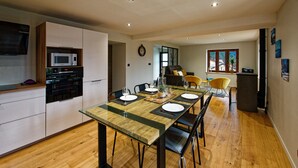 A modern kitchen with a dining area, wooden flooring, and a view of the outdoors. - Cosy*SPA*Modern- at Ô JurassiK (Coteaux du Lizon)