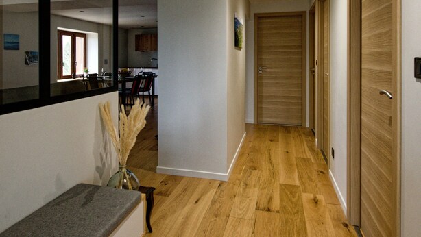 A hallway with wooden flooring, a bench, a mirror, and a door at the end. - Cosy*SPA*Modern- at Ô JurassiK (Coteaux du Lizon)