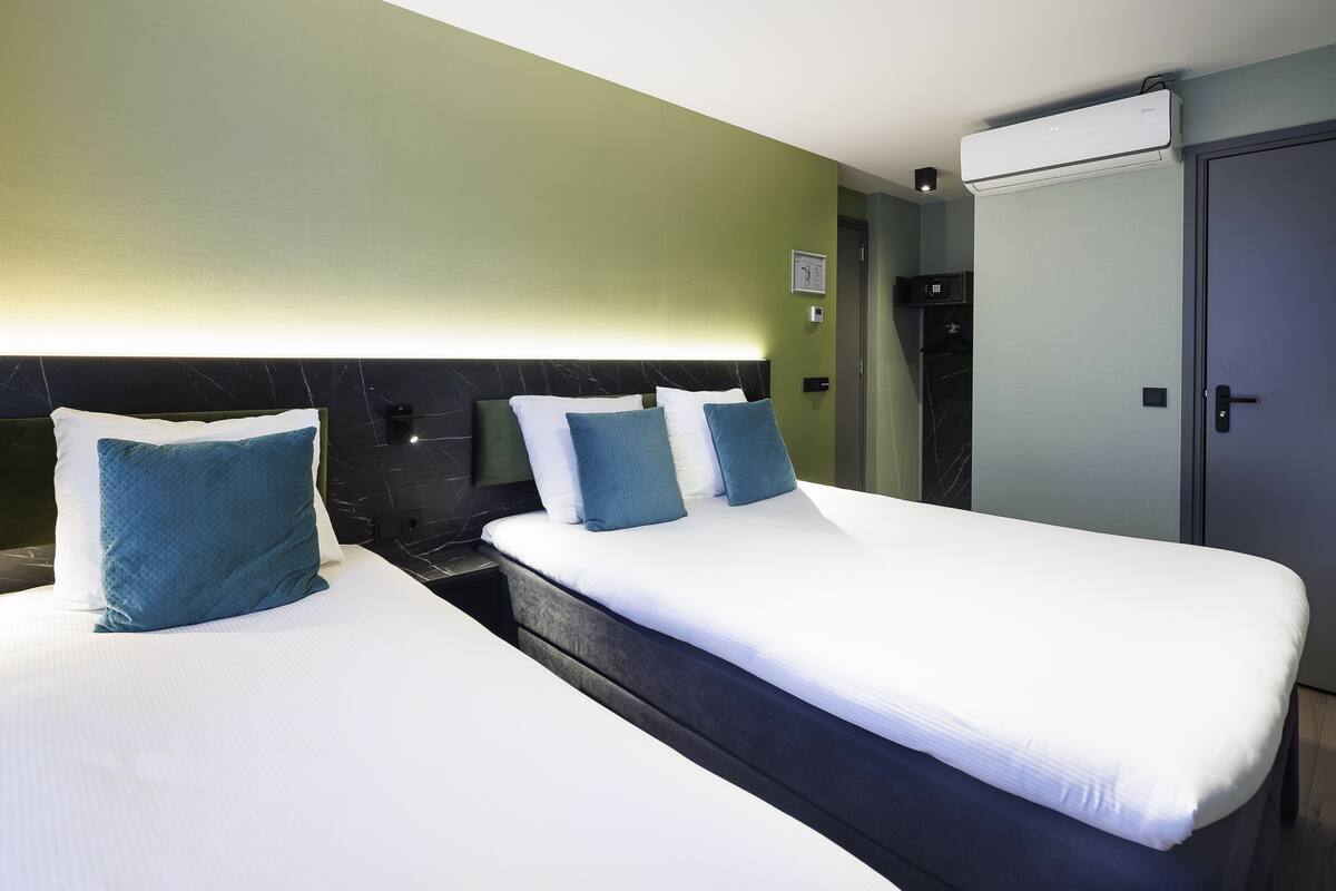 Una habitación de hotel con dos camas, un minibar, un armario y un equipo de aire acondicionado instalado en la pared.