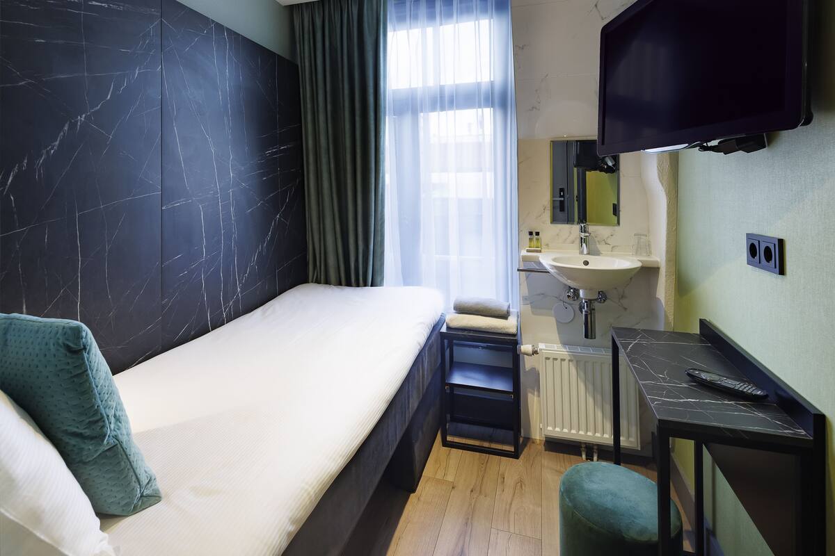 Habitación de hotel con cama, un escritorio pequeño, un espejo, un lavamanos y una ventana con cortinas.