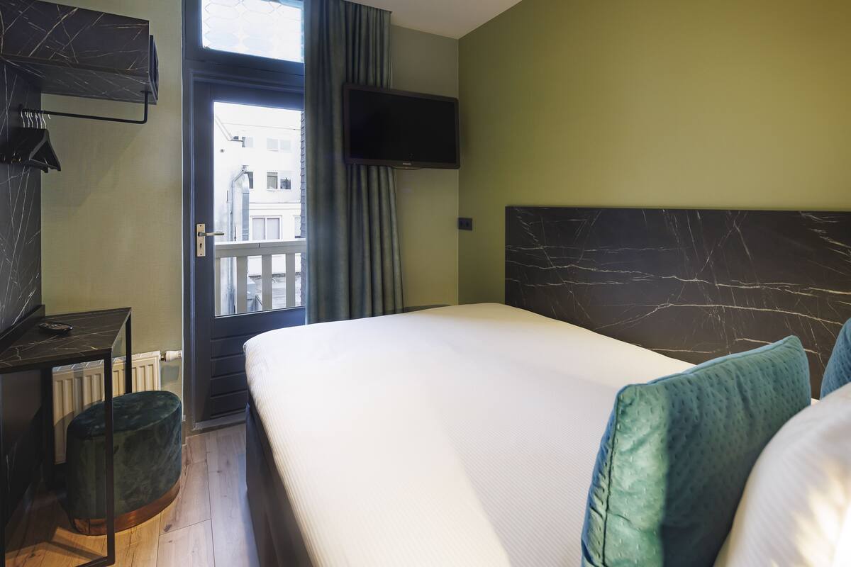 Una habitación de hotel con cama, escritorio, televisión y vista al exterior.