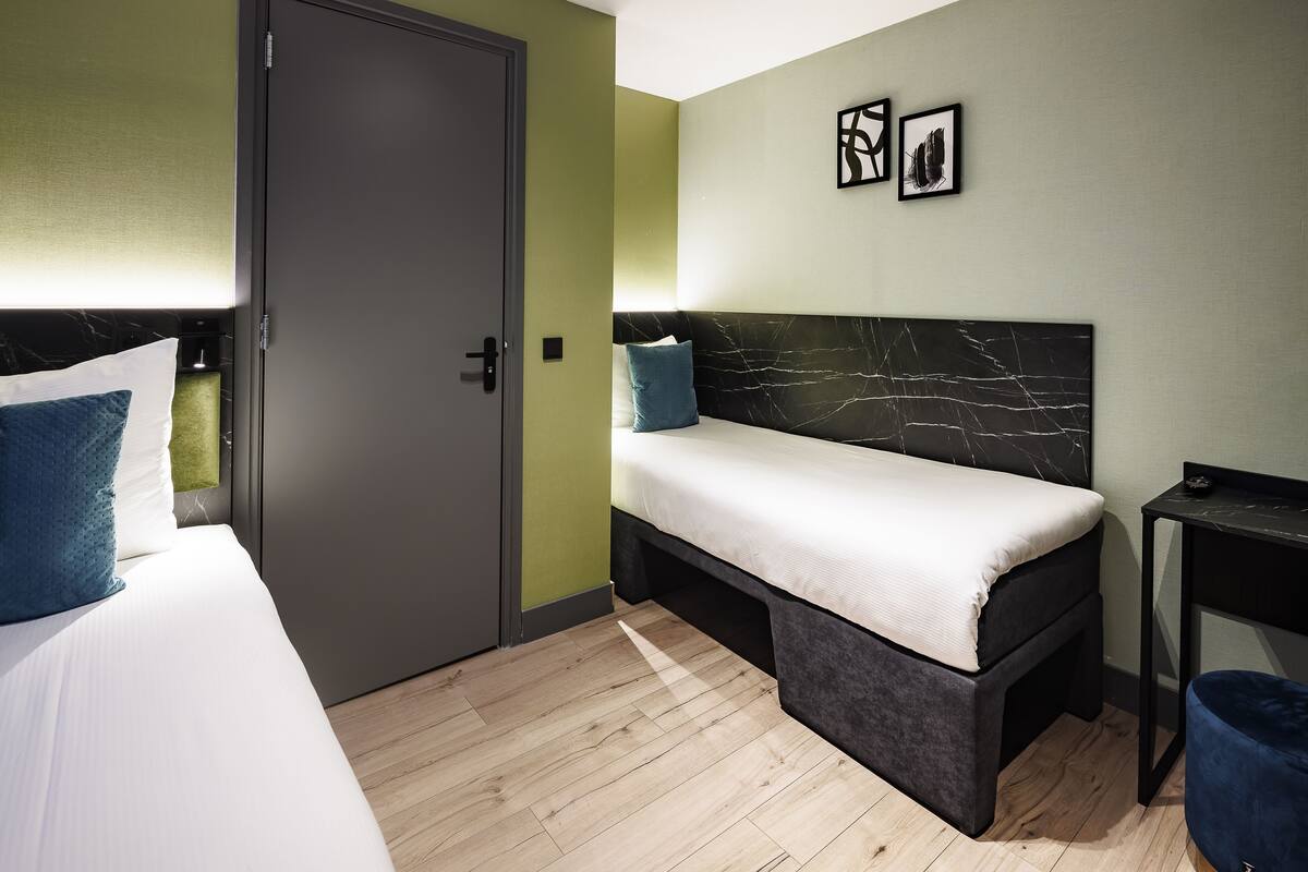 Una habitación de hotel compacta con una cama, un pequeño sofá, un escritorio y un armario.