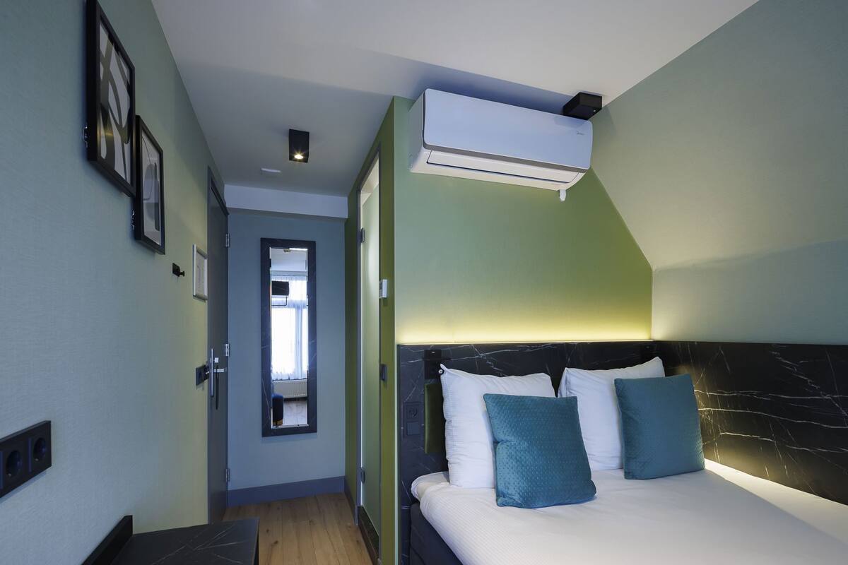 Habitación de hotel con cama, unidad de aire acondicionado, pasillo y puerta que da a otra habitación.