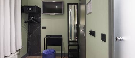 A compact hotel room with a bed, a TV mounted on the wall, a small table, a mirror, and a wardrobe.