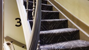Un escalier en colimaçon avec le chiffre « 3 » peint sur le mur, des marches recouvertes de moquette et une main courante.