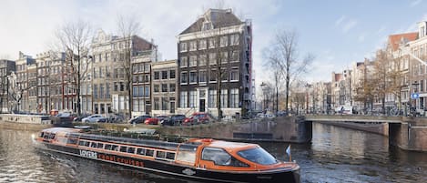 A canal cruise boat named 'Lovers' with a black and orange exterior, navigating through a canal lined with historic buildings.