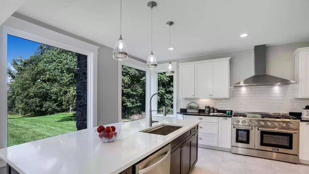 A modern kitchen with a large island, stainless steel appliances, and a view of a green landscape.