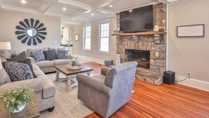 A living room with a stone fireplace, a flat-screen TV, and a modern ceiling design.