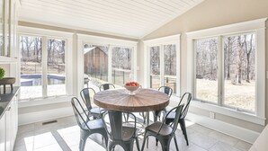 A sunroom with a round table and chairs, large windows, and a view of a backyard.