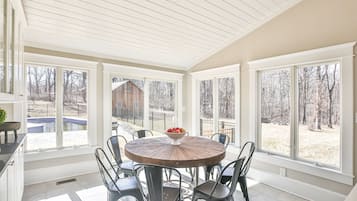Une véranda avec une table ronde et des chaises, de grandes fenêtres et une vue sur le jardin arrière.