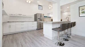 A modern kitchen with white cabinetry, stainless steel appliances, and a bar area with stools. - 4/5 for 8, Steps to Beach-Jacuzzi, Furnished Patio (Hollywood)