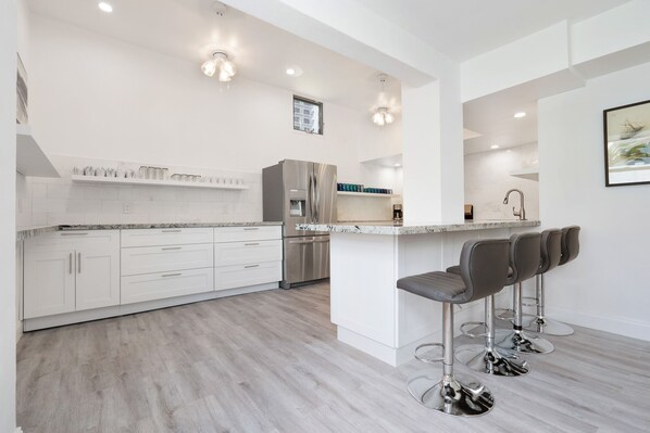 A modern kitchen with white cabinetry, stainless steel appliances, and a bar area with stools.